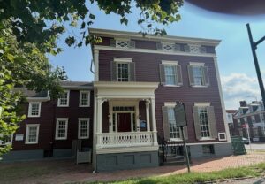 Front view of the historic Lee-Fendall House in Alexandria, Virginia, a red-painted 18th-century residence with white trim and a porch, now preserved as a museum.