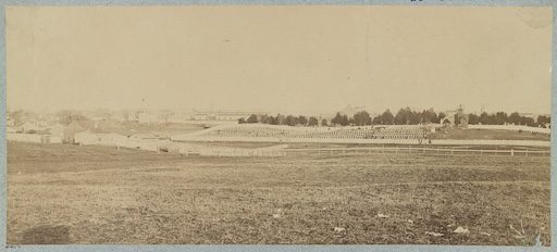 Historic 1865 photograph of Alexandria National Cemetery taken from West Village across Hooff’s Run. The cemetery’s entrance arch is visible in the distance, though its inscription cannot be read from this angle. A large open field dominates the foreground, reflecting the undeveloped landscape surrounding the cemetery at the time. The vantage point is likely near the 1800 block of Jamieson Avenue, along the former route of the Orange & Alexandria Railroad. Image courtesy of the Library of Congress.