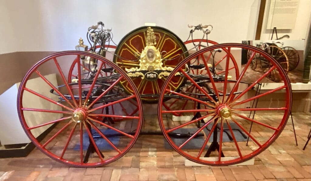 Immaculately restored 19th-century hose-reel carriage with wooden wheels and polished brass fittings, displayed inside the Friendship Firehouse Museum in Alexandria, Virginia.