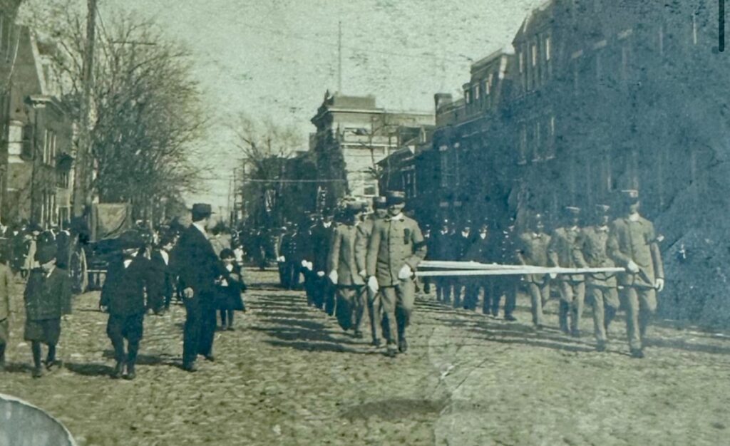 Crowds of people stand along city sidewalks and gather at the cemetery as the funeral procession for Fire Chief George W. Petty passes, paying tribute to the late fire chief.