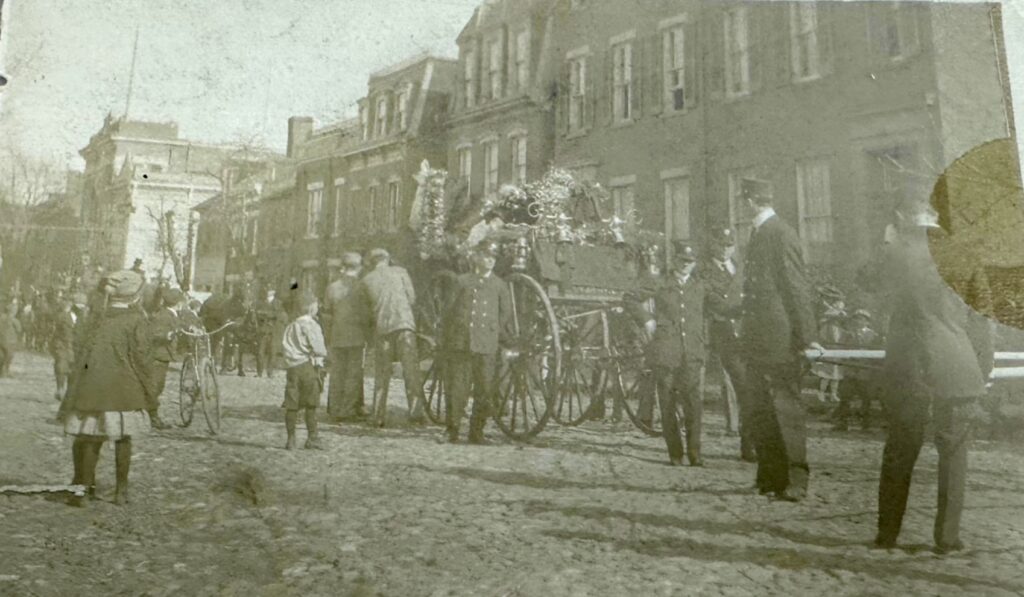 Horse and fire cart led by a volunteer fireman, carrying the helmet, coat, and boots of Fire Chief George W. Petty during his funeral procession.