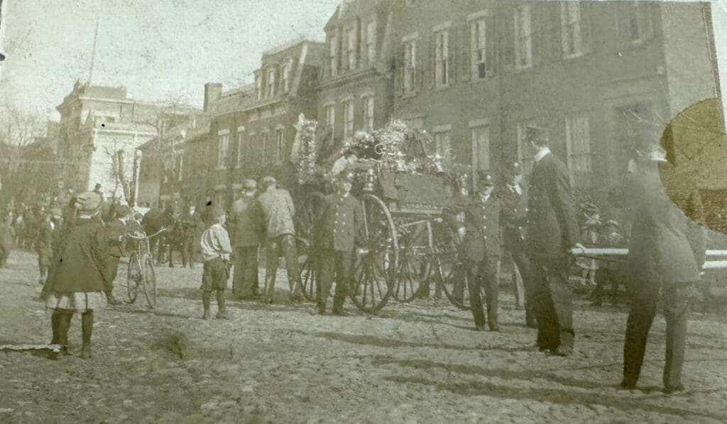 Horse and fire cart led by a volunteer fireman, carrying the helmet, coat, and boots of Fire Chief George W. Petty during his funeral procession.