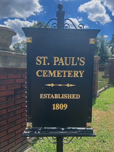 Black metal sign with gold lettering reading “St. Paul’s Cemetery – Established 1809,” located at the entrance of St. Paul’s Episcopal Cemetery in Alexandria, Virginia.