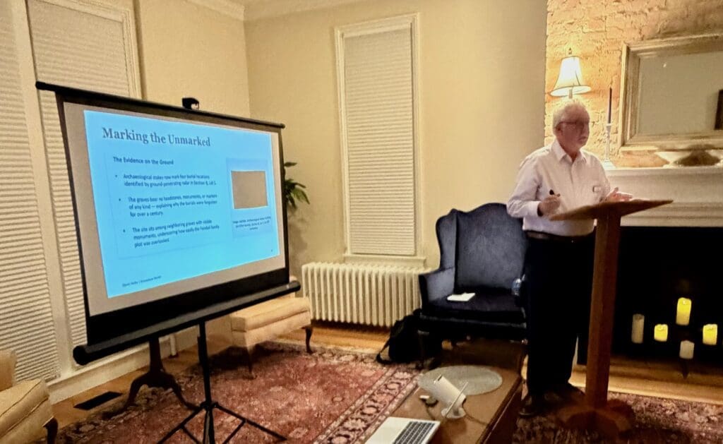 Public historian David Heiby presenting a lecture at Ivy Hill Cemetery’s 170th anniversary event, standing at a podium beside a projected slide titled “Marking the Unmarked.”