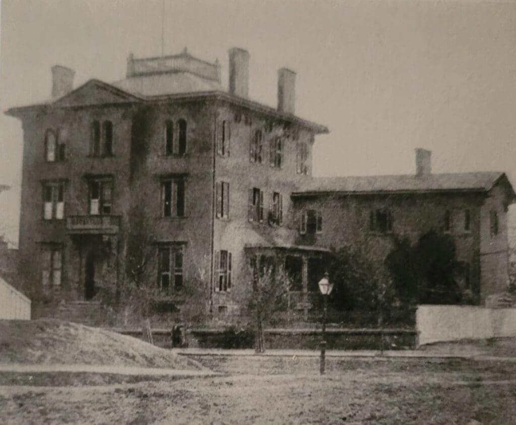 Grayscale photo of a multi-story brick building with many windows and a flat roof, urban street scene.